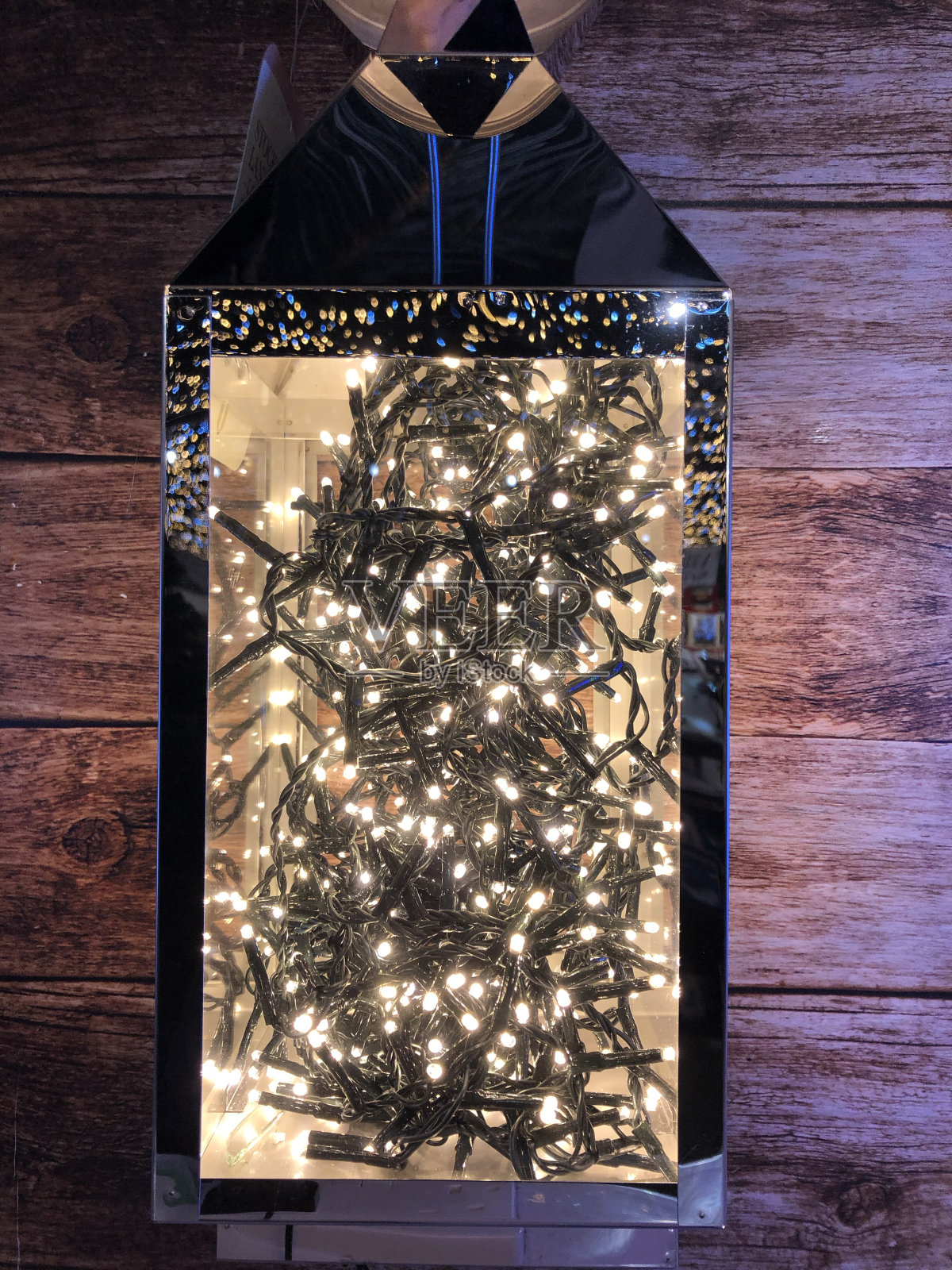 一个展示盒的特写图像，铬和玻璃包含一团白色LED仙女灯，木纹背景照片摄影图片