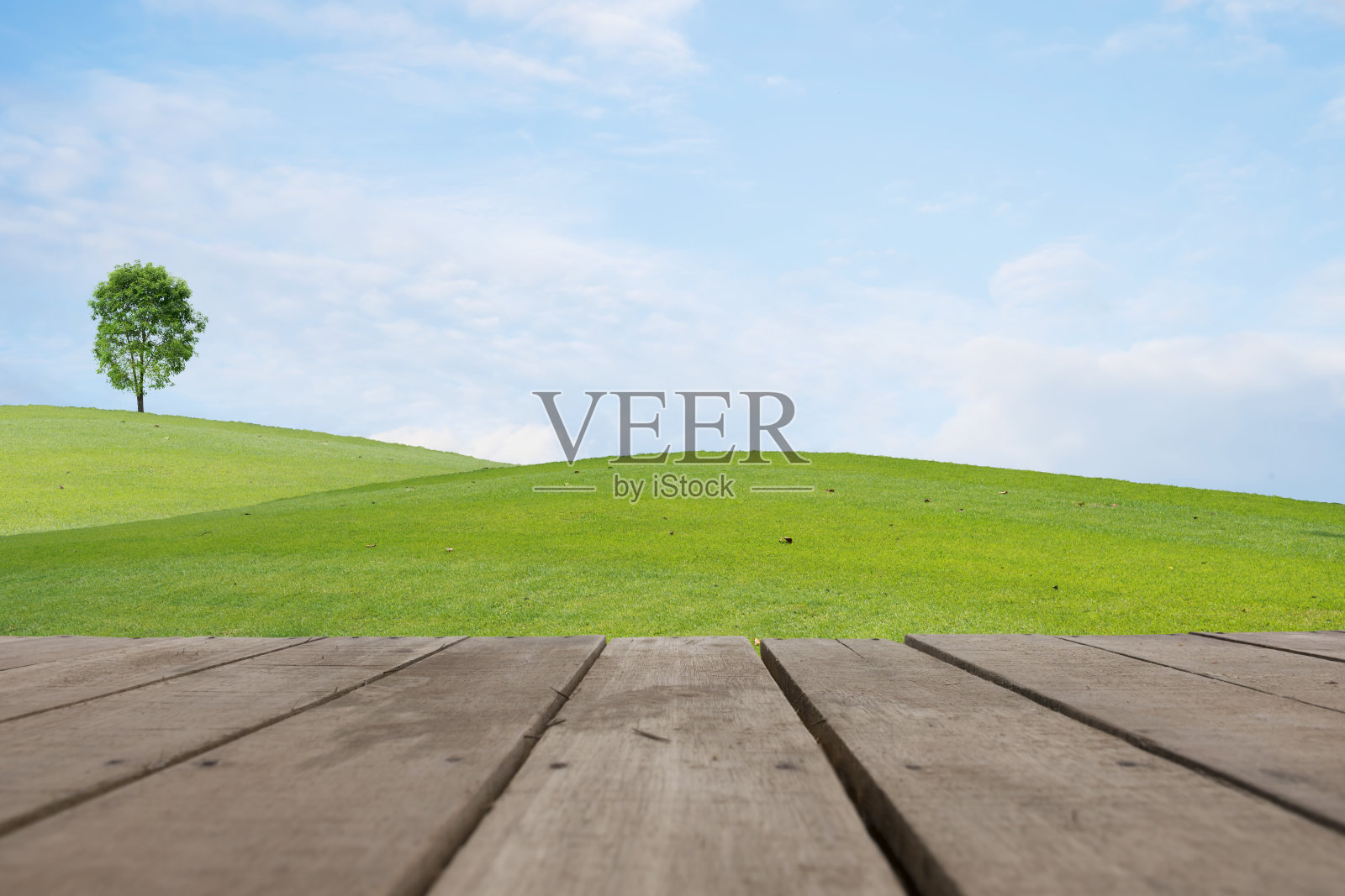 木地板在美丽的绿色草地上，山上有白云，蓝天和树木照片摄影图片
