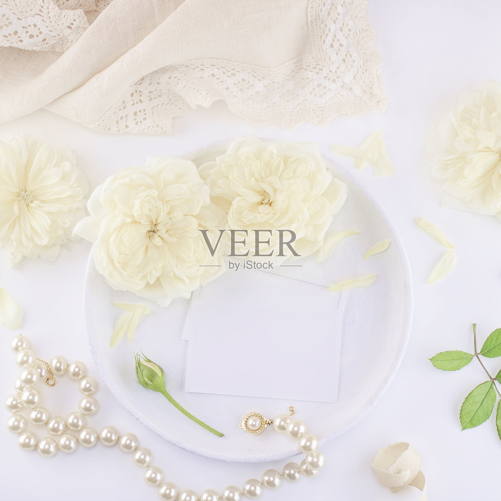名片模型放在白色盘子上，上面有玫瑰和珍珠项链。婚礼或生日邀请函。女性化的风格照片摄影图片