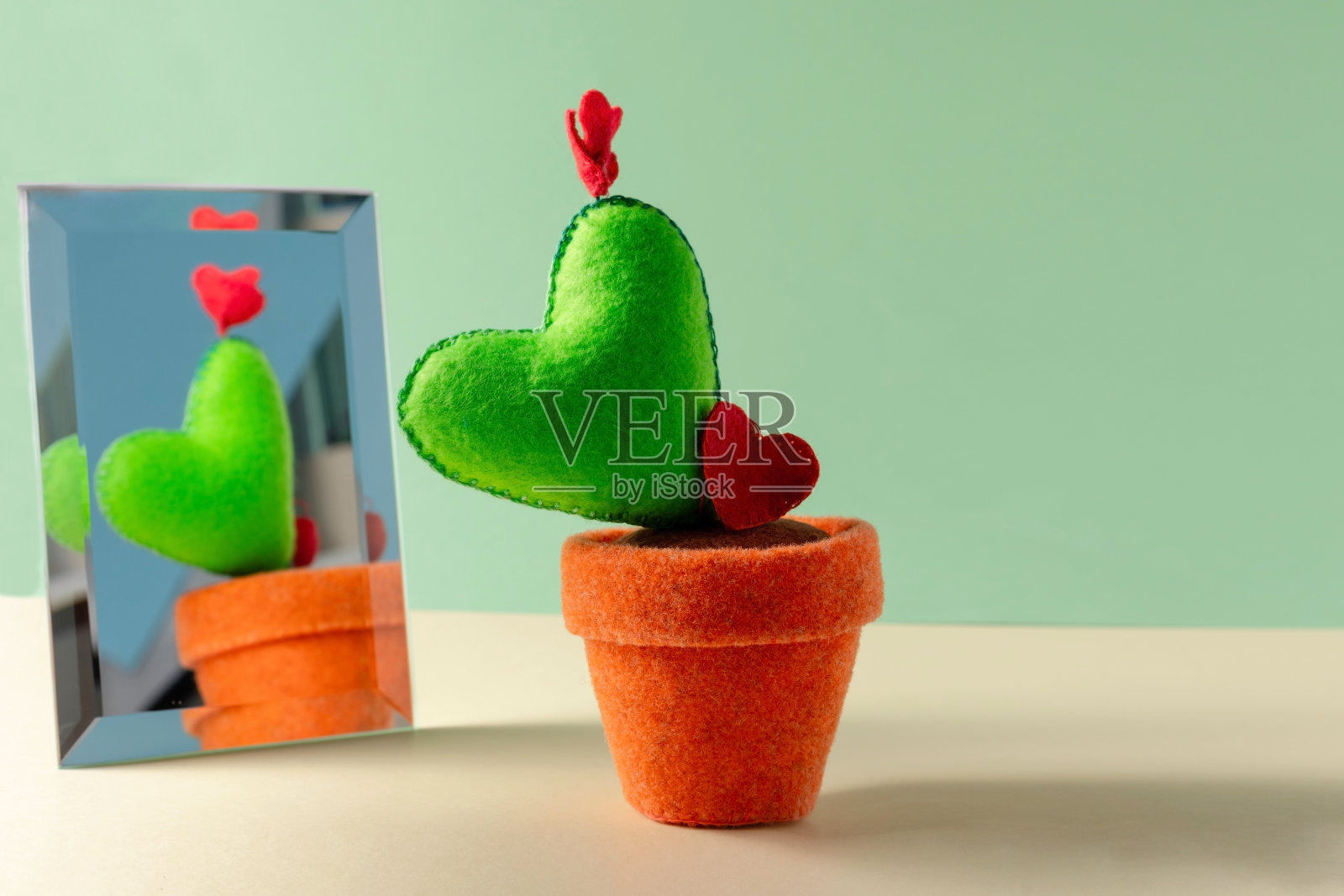 这个玩具是用毛毡制成的绿色心形植物放在靠近镜子的花盆里。针线活的概念，情人节卡片，求婚。照片摄影图片