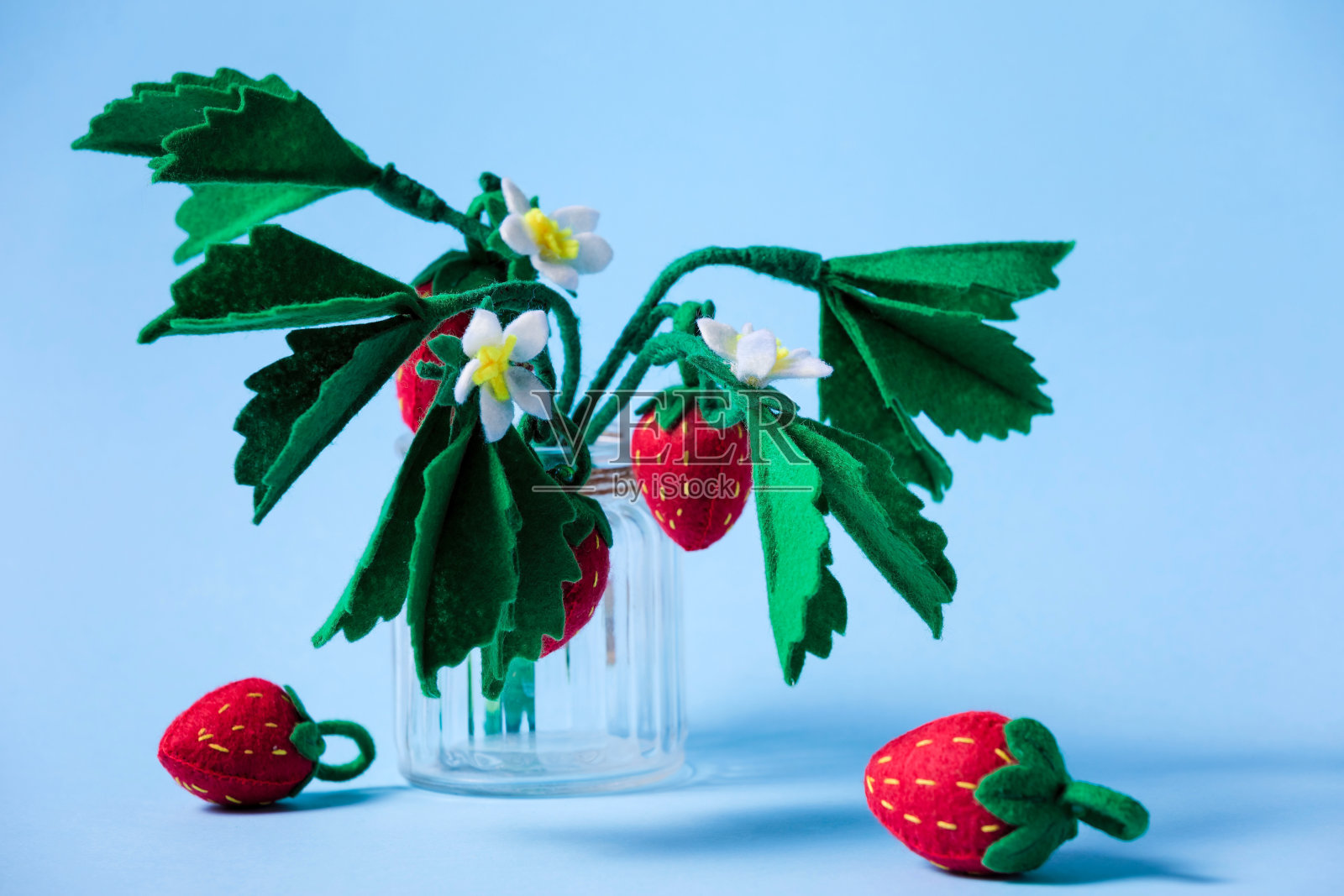 夏日里，蓝色背景上是手工制作的盛开的草莓丛。上手。照片摄影图片