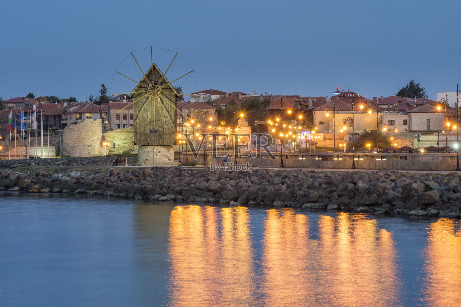 夕阳下古老的风车和城市的灯光。照片摄影图片