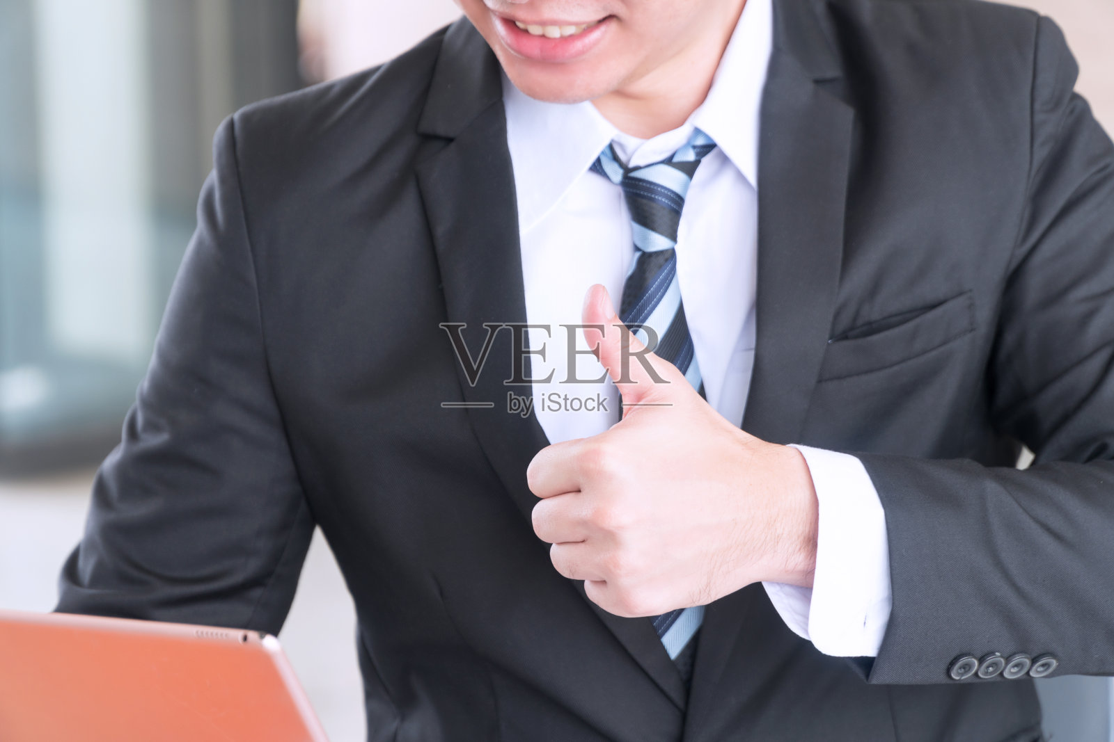 商人在为一份好工作工作时竖起了大拇指。年轻人穿着西装，翘起大拇指代表商业成功，好，很棒，所有的好东西。商业成功的概念。照片摄影图片