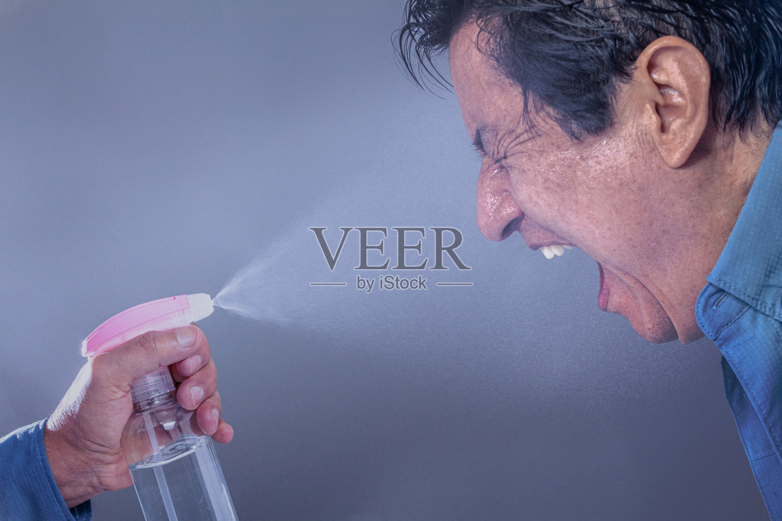 拿着酒精凝胶机往一名男子脸上喷洒消毒剂。照片摄影图片