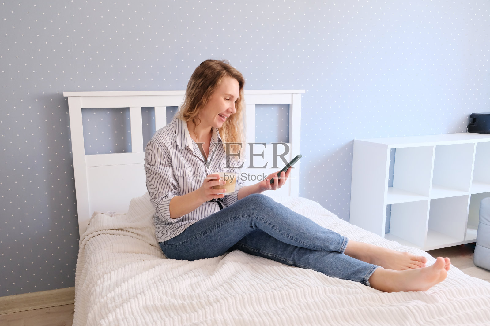 一名年轻女子坐在床上一边喝咖啡一边讲手机照片摄影图片