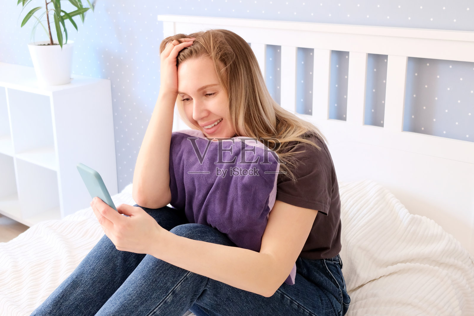 一个漂亮的女人坐在床上，手里拿着一部智能手机照片摄影图片
