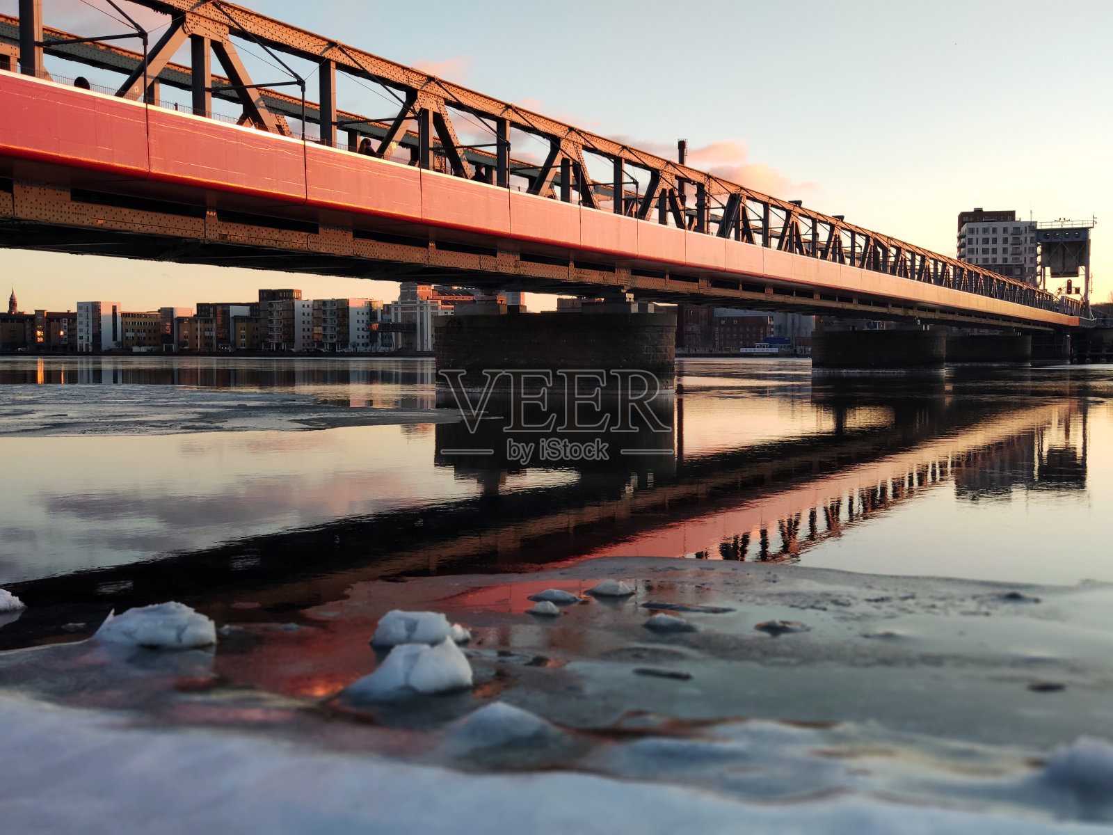 丹麦日落时冰冻的水面上的红色人行天桥照片摄影图片