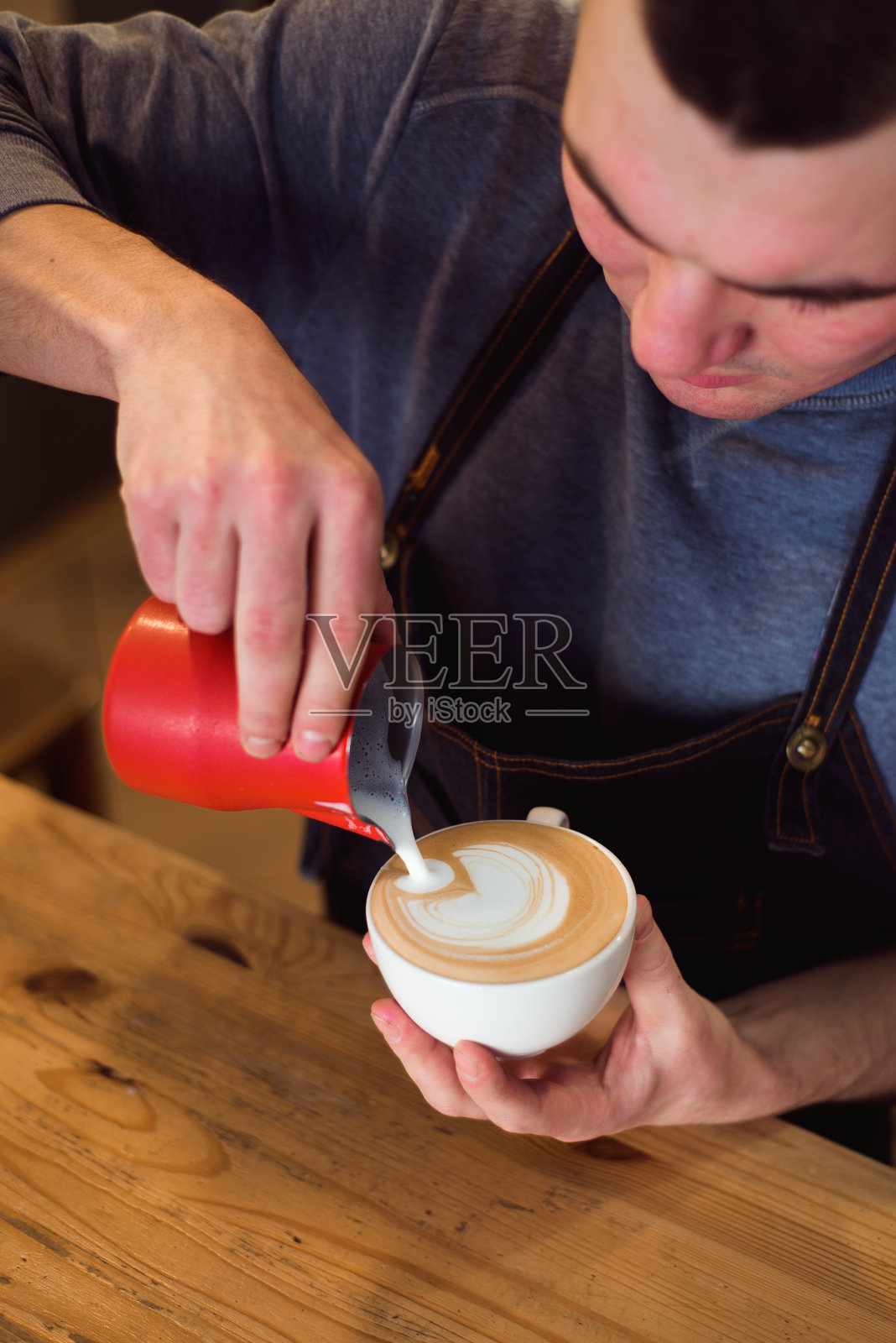 咖啡师将牛奶倒入咖啡杯中，制作拉花艺术。照片摄影图片