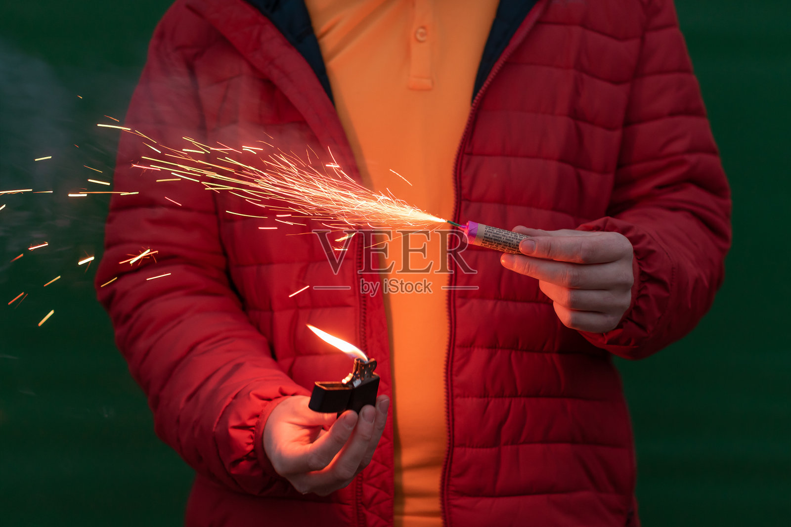 穿红夹克的男人在他的手中点燃鞭炮照片摄影图片