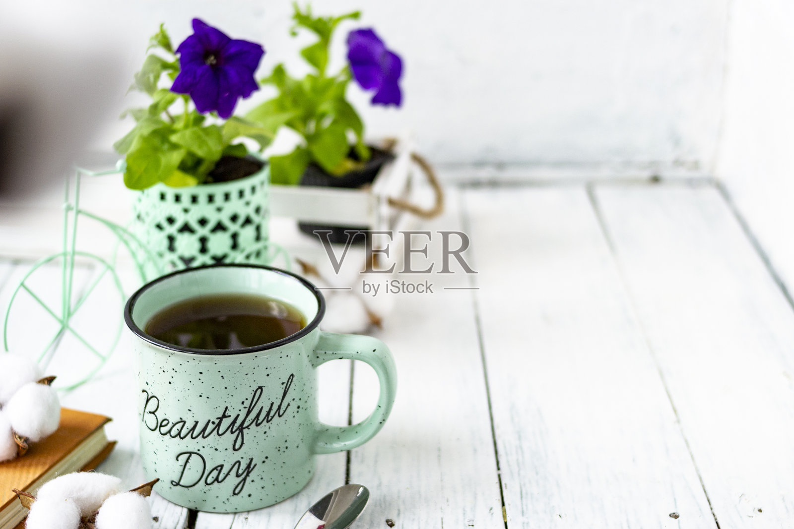 特写一杯茶在一个木制的白色桌子上模糊的背景，前面模糊。静物有花，书，茶匙，棉盒。春天的早餐。副本的空间。照片摄影图片
