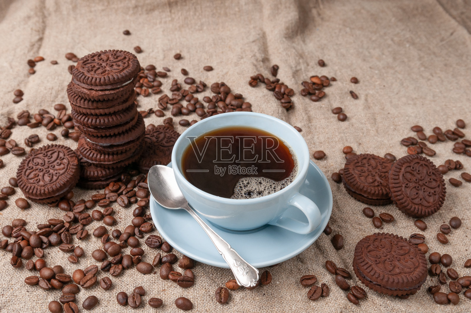 蓝色杯子里的咖啡。附近有巧克力饼干。用咖啡豆装饰。灰色亚麻背景。照片摄影图片