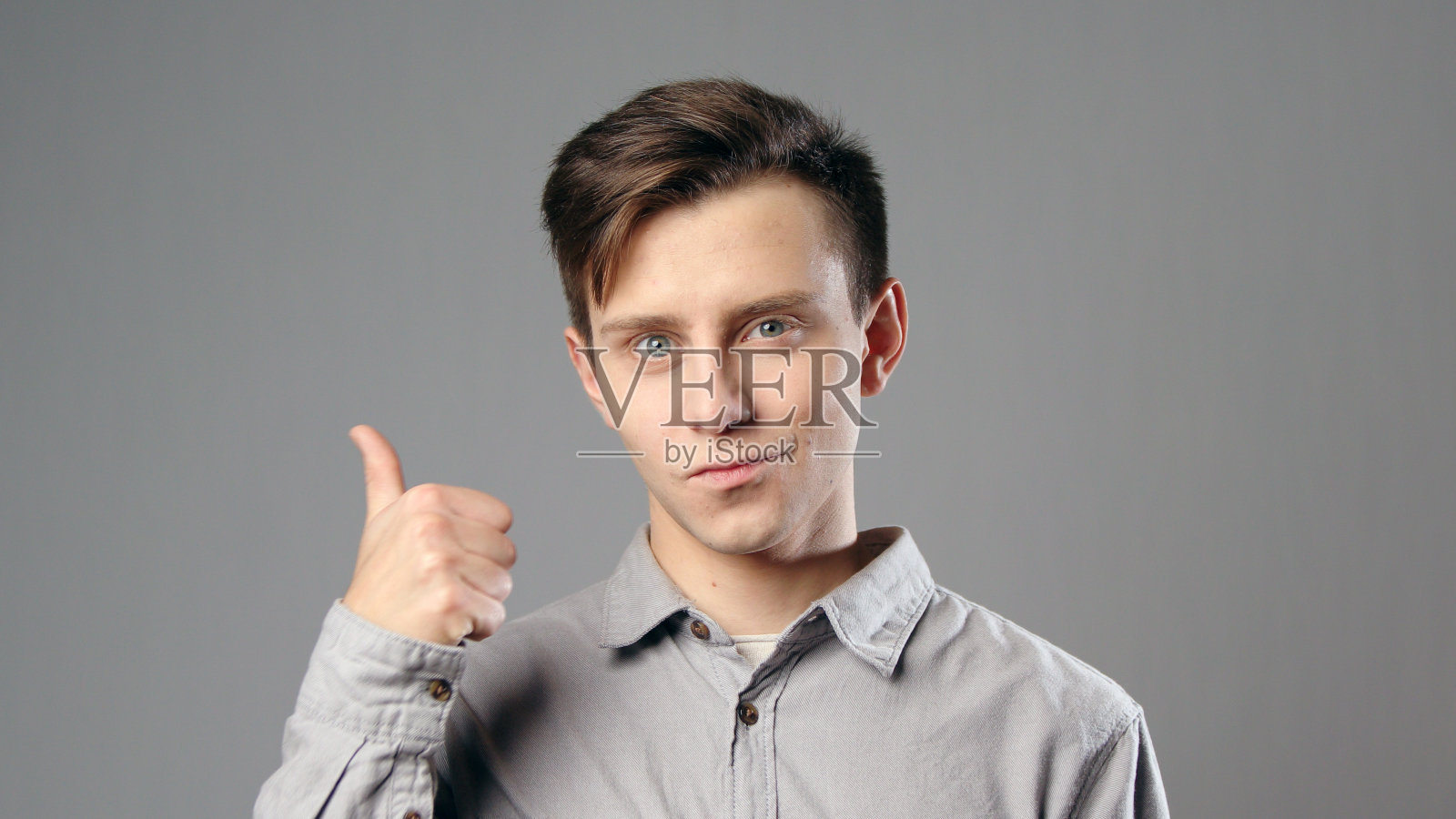 白人男子拇指上升穿着灰色衬衫在灰色背景照片摄影图片