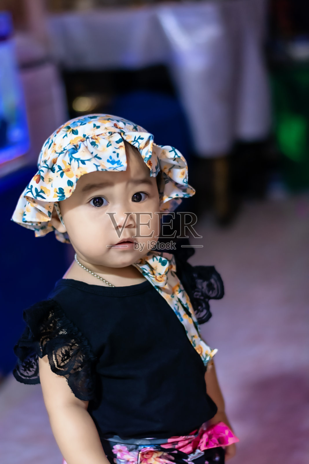 近距离的可爱的微笑的小女孩微笑着看着相机。快乐的亚洲小女孩戴着漂亮的帽子和黑色的衣服，享受和玩在家里的家人。照片摄影图片