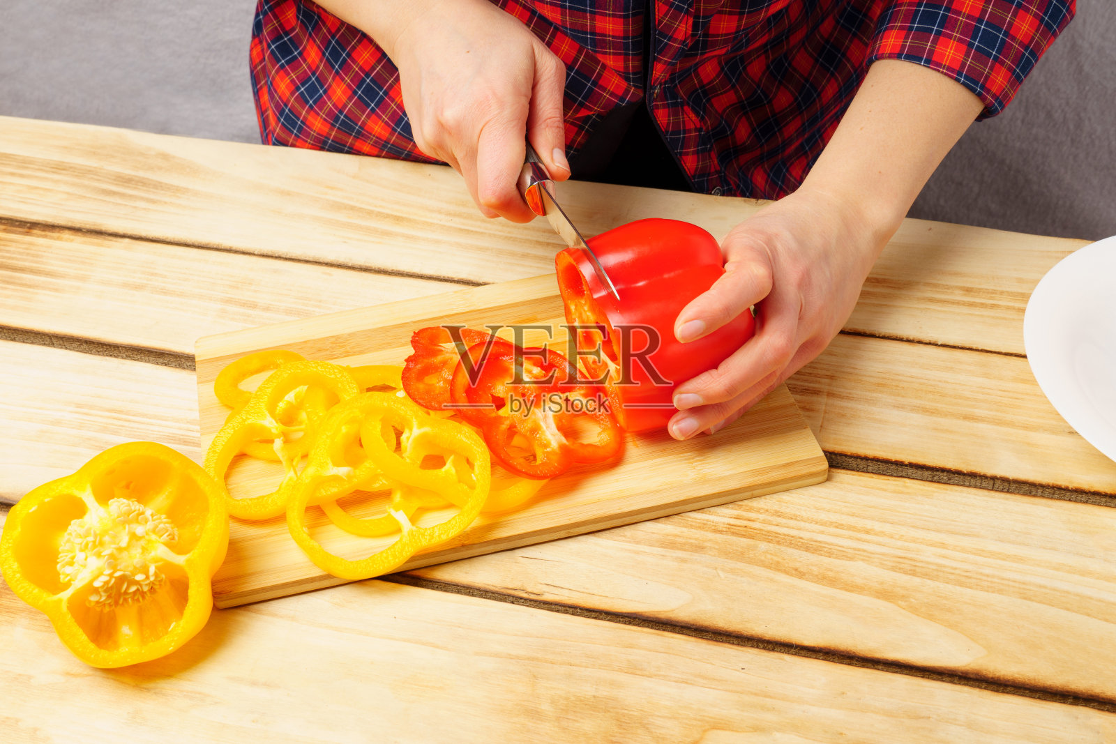 切蔬菜做新鲜的沙拉。一位年轻的家庭主妇在木桌旁的砧板上切青椒。照片摄影图片