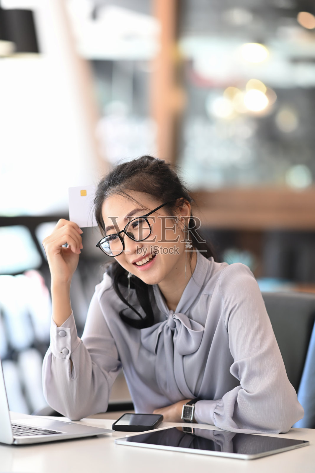 一幅欢快的年轻女子的肖像，戴着眼镜，用笔记本电脑和信用卡进行网上支付或网上购物。照片摄影图片