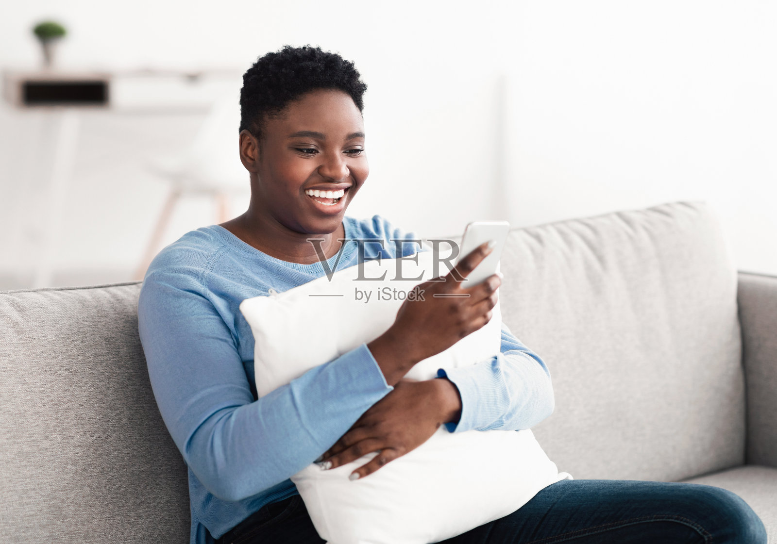 微笑的黑人妇女用手机，抱着枕头照片摄影图片