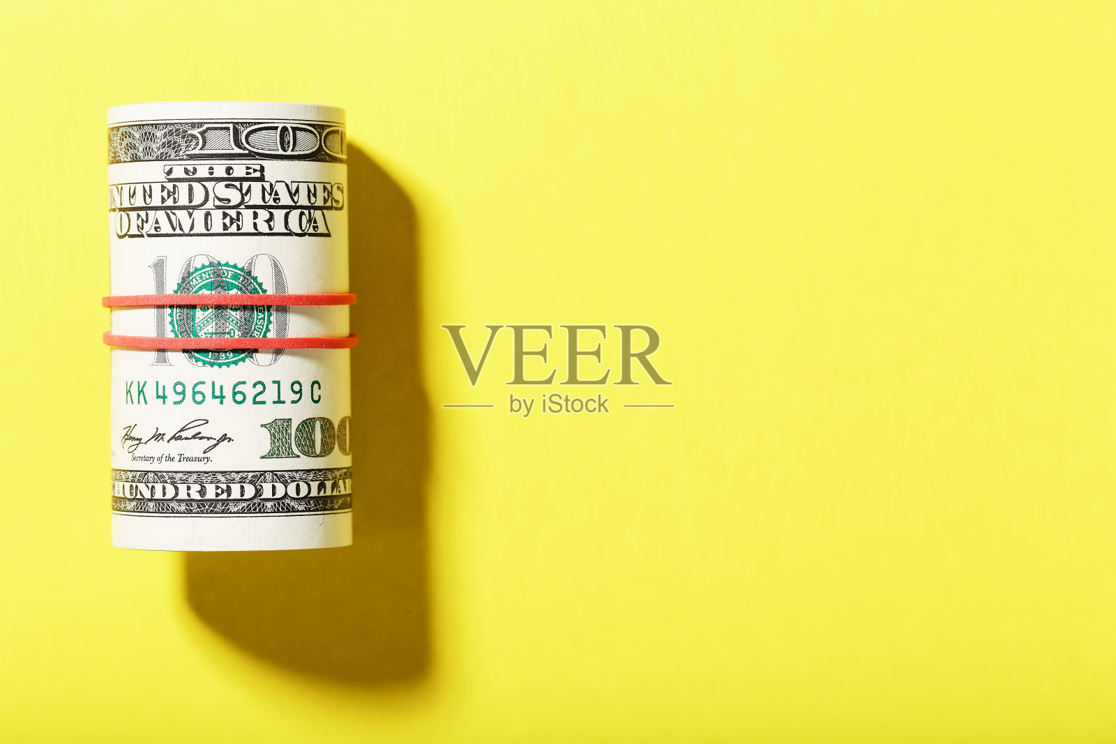 一卷百元美钞用红色橡皮筋捆在黄色背景上。照片摄影图片