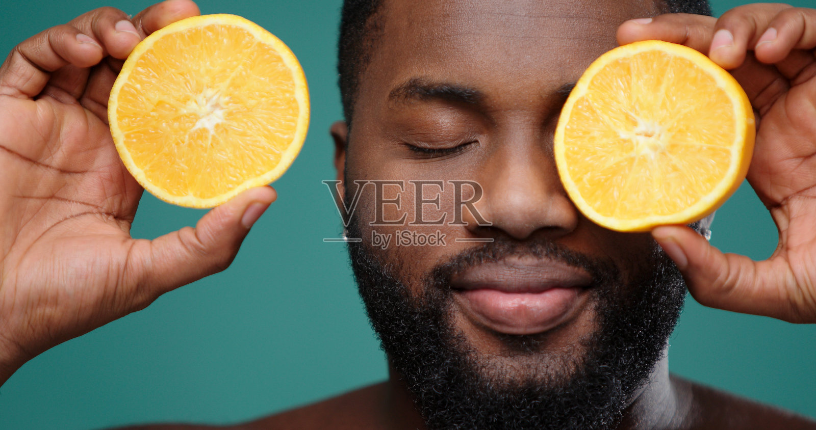 一个非裔美国人拿着橘子片，给眼睛带来视觉照片摄影图片