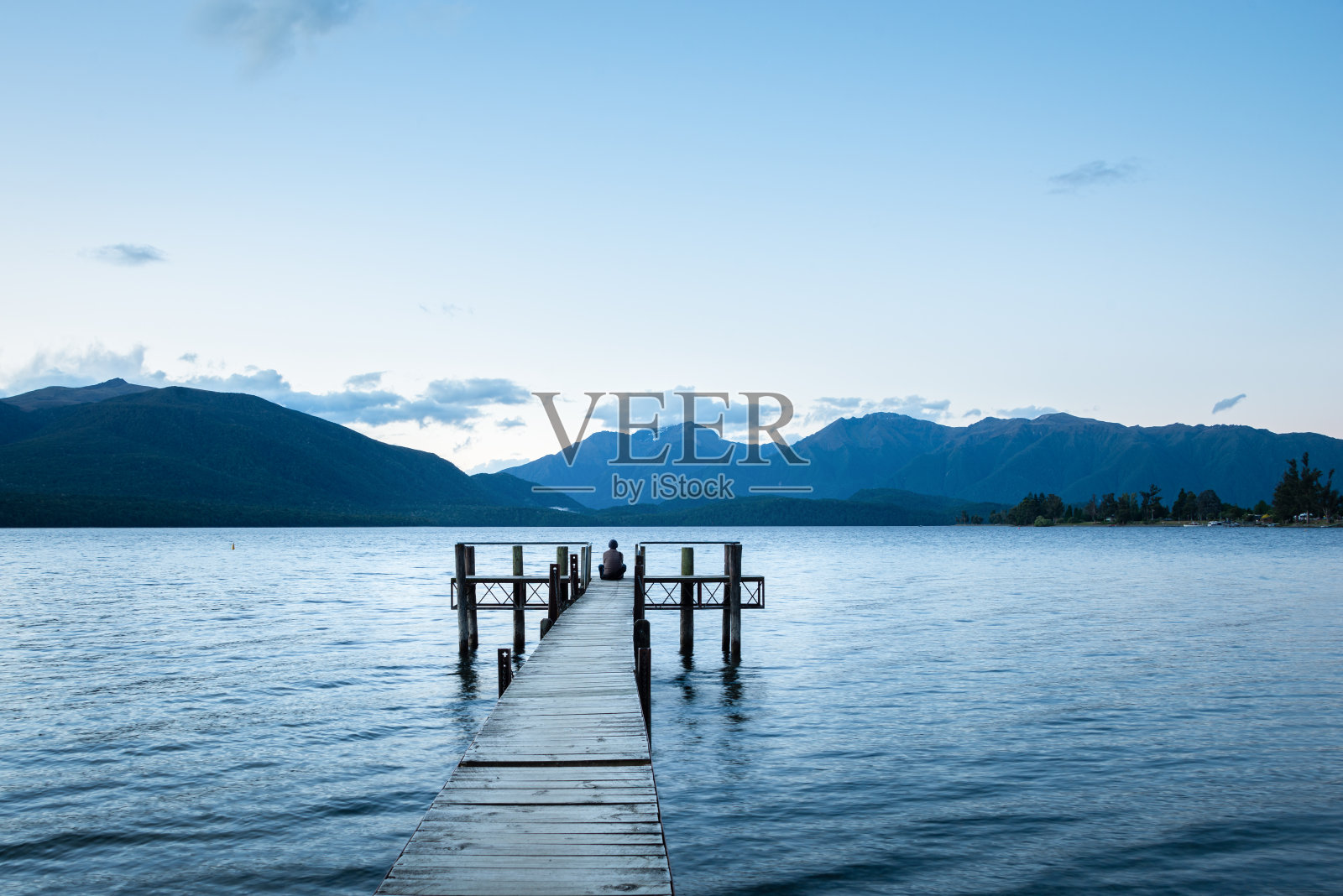 一个孤独的男人坐在特阿瑙湖码头的尽头，看着南岛的开普勒山脉照片摄影图片