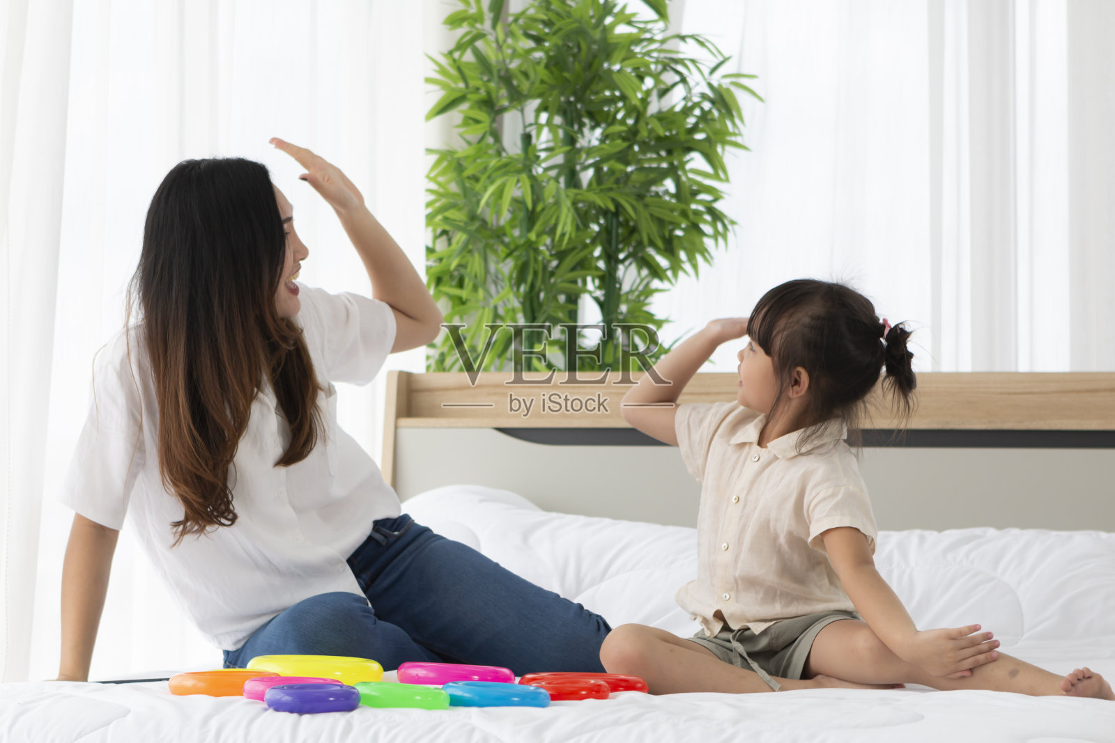 妈妈和女儿在床上打了个招呼，早上他们在一起玩。在家庭隔离期间，母亲和女儿坐在床上打手势，一起玩游戏。照片摄影图片