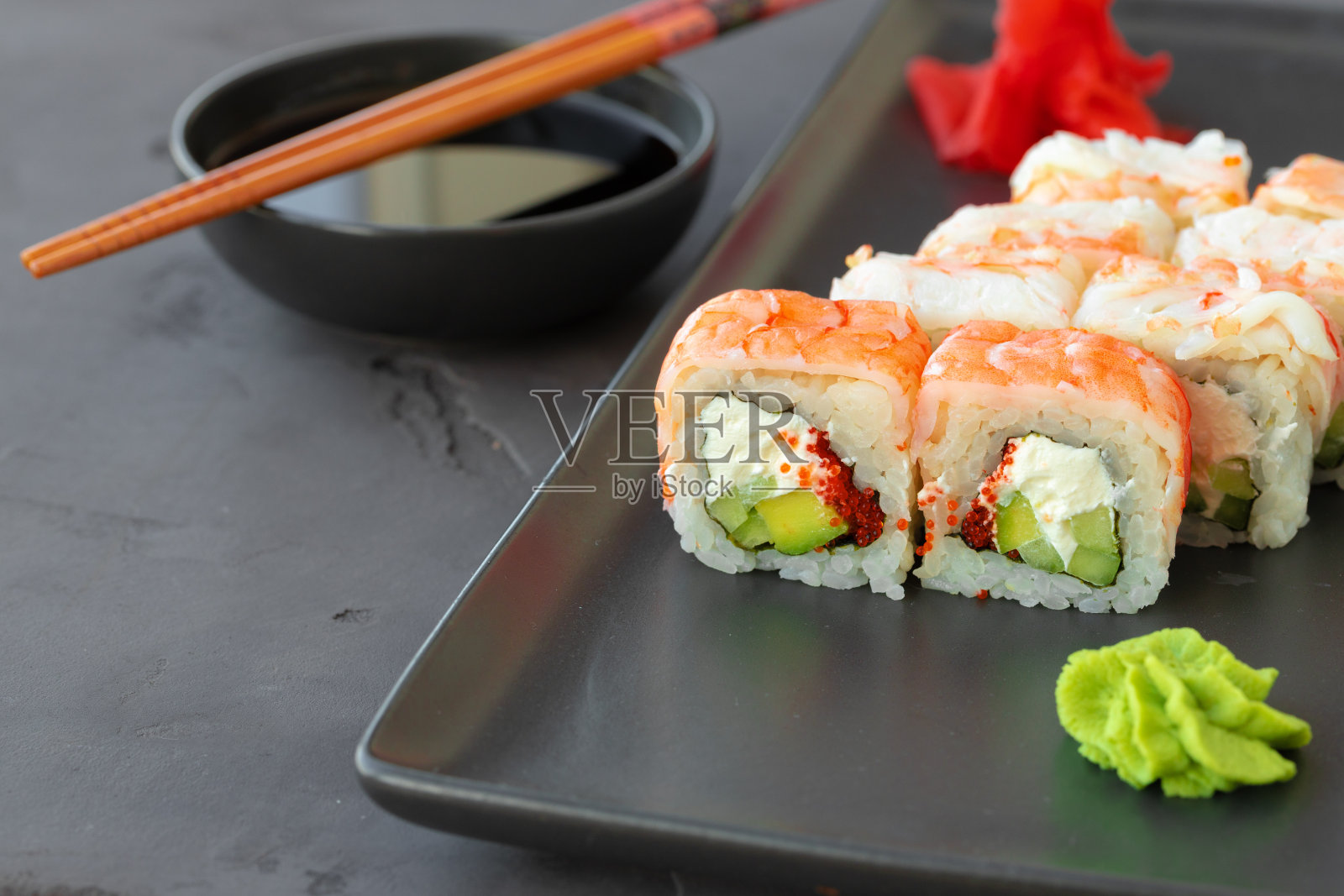 寿司卷上覆有虾肉，放在黑色陶瓷盘上照片摄影图片