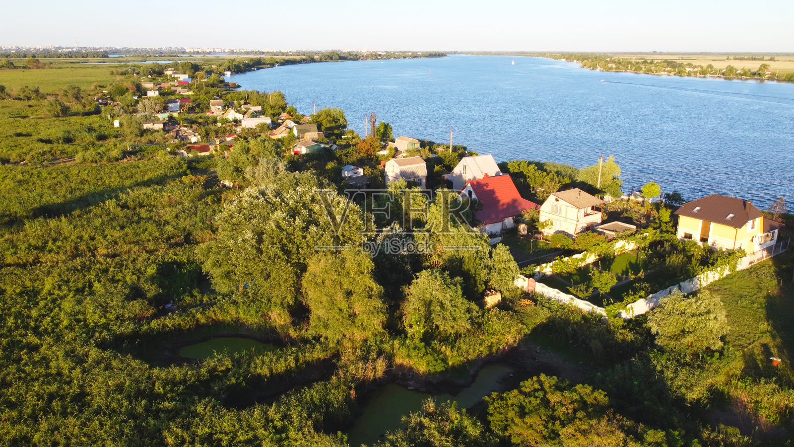 无人机飞过波浪起伏的河流，周围是当地的村庄，有各种各样的建筑和湿地和沼泽栖息地，芦苇床鸟瞰图。前视图。照片摄影图片