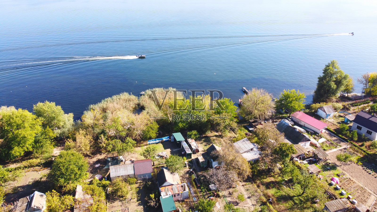 无人机飞过波浪起伏的河流，周围是当地的村庄，有各种各样的建筑和湿地和沼泽栖息地，芦苇床鸟瞰图。前视图。照片摄影图片