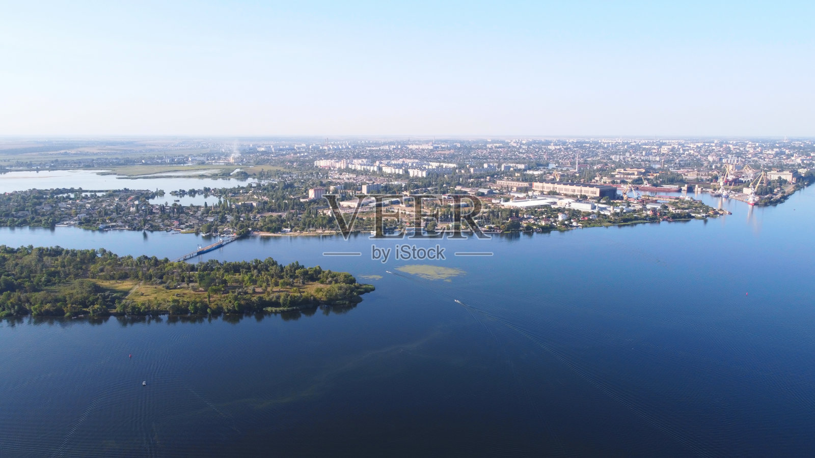 无人机飞过波浪起伏的河流，周围是当地的村庄，有各种各样的建筑和湿地和沼泽栖息地，芦苇床鸟瞰图。前视图。照片摄影图片