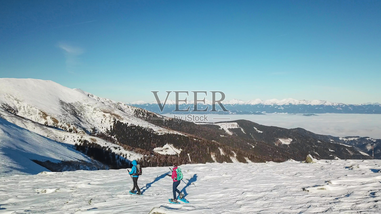 speikogel -无人机拍摄的一对夫妇穿着雪地鞋攀登奥地利阿尔卑斯山Amerinkogel峰。新鲜的粉雪照片摄影图片