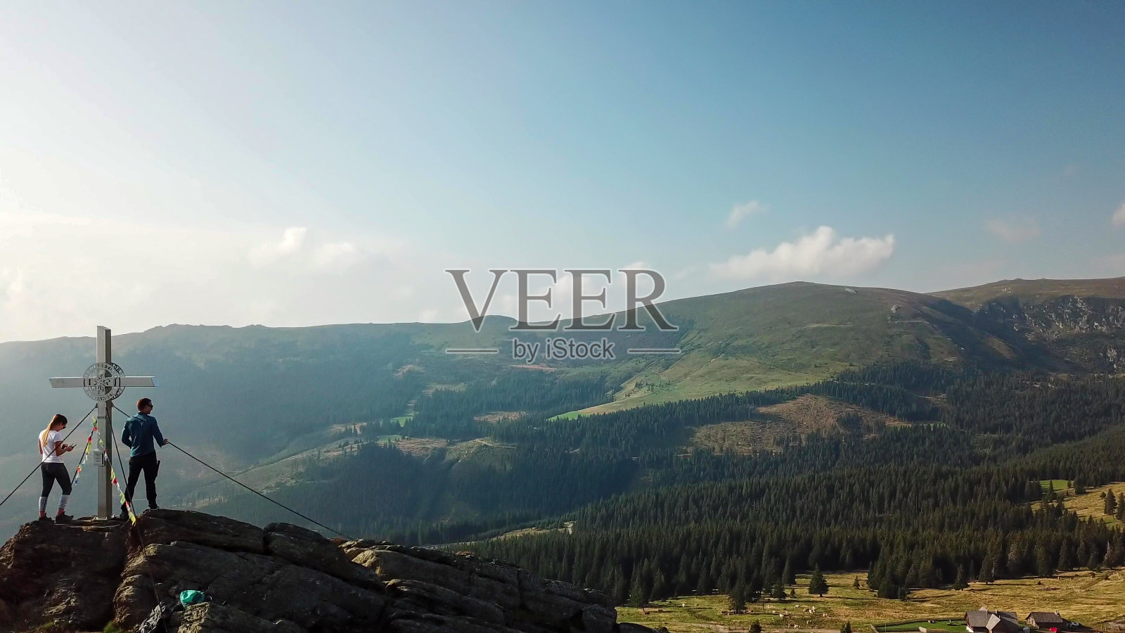 speikogel -无人机拍摄的一对夫妇站在Loskogel山顶，旁边是奥地利阿尔卑斯山的一个十字架。松软的丘陵和山脉照片摄影图片