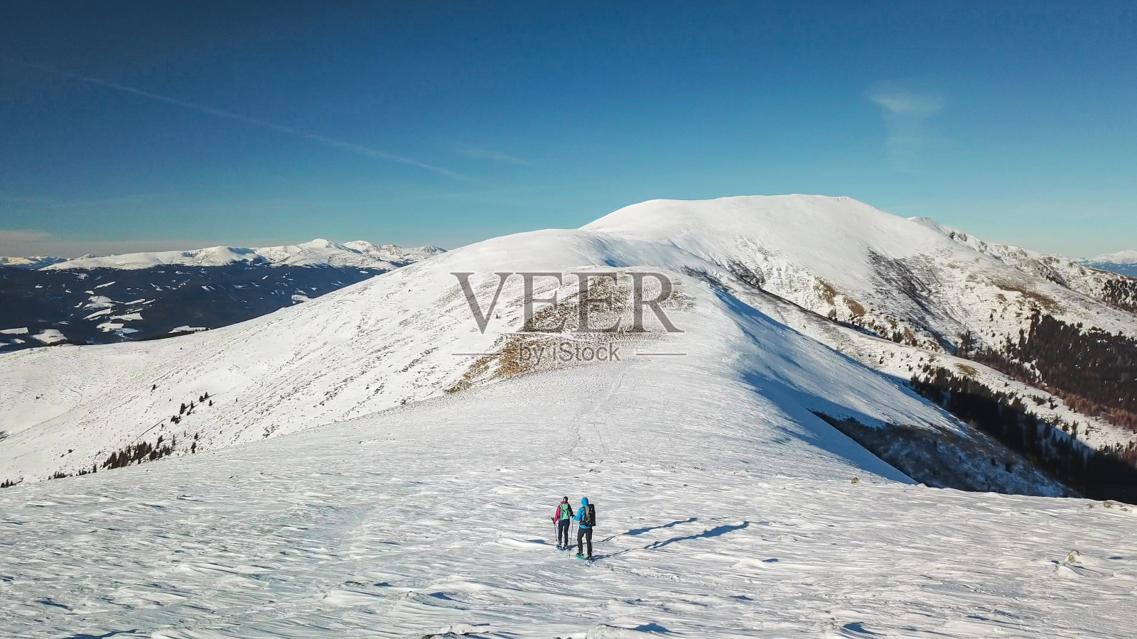 speikogel -无人机拍摄的一对夫妇穿着雪地鞋攀登奥地利阿尔卑斯山Amerinkogel峰。新鲜的粉雪照片摄影图片