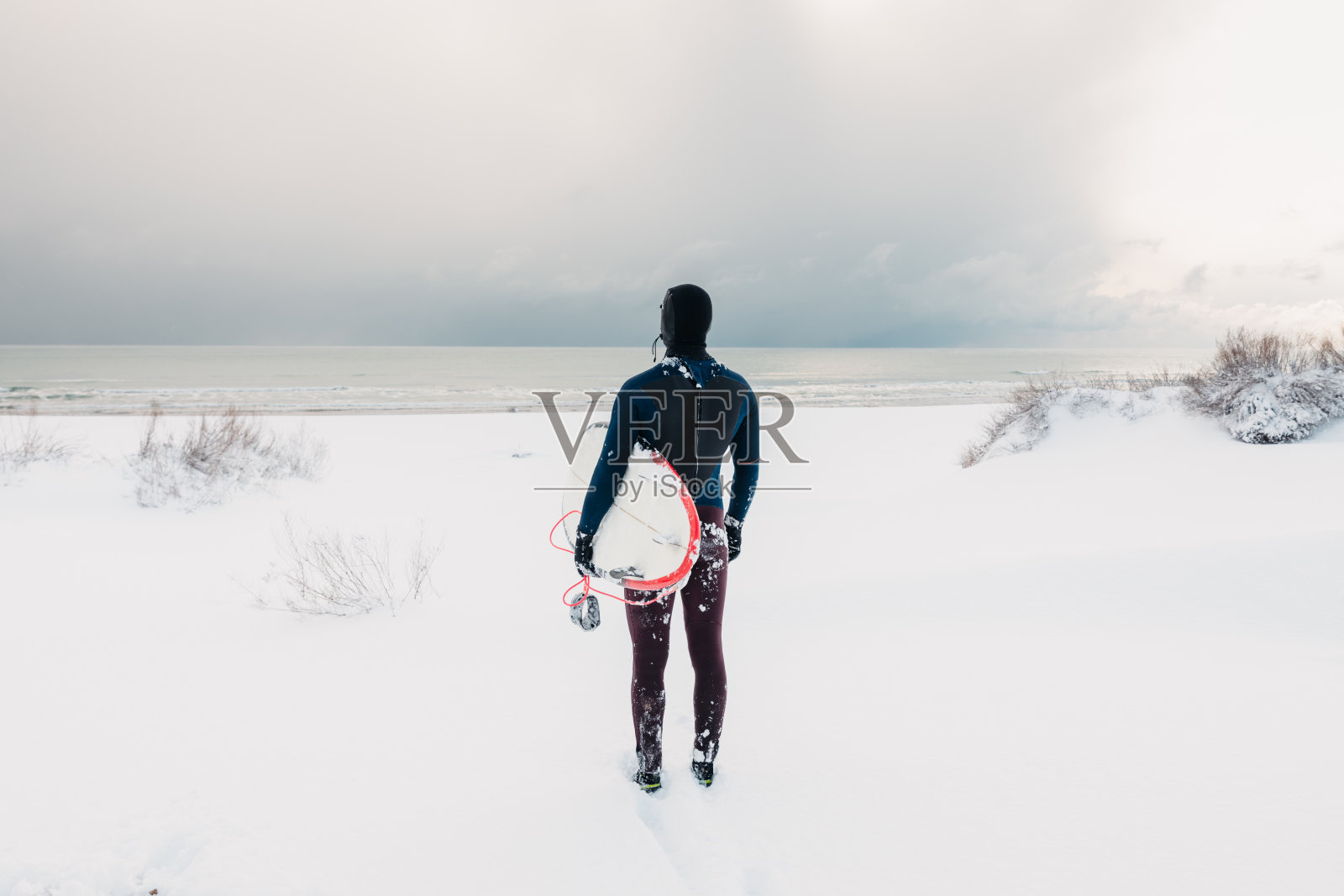 下雪的冬天和冲浪板。穿着潜水服的冬季海滩和冲浪运动员。照片摄影图片