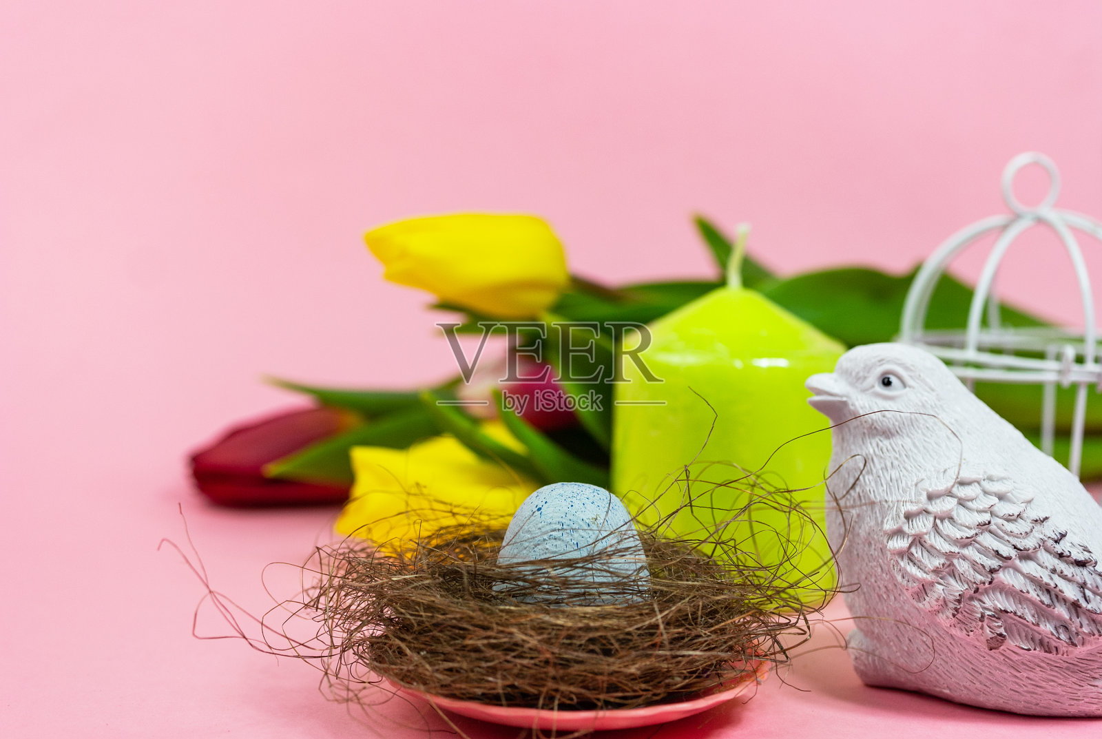 春天的明信片。复活节彩蛋在一个有苔藓的巢里，一只鸟，一个笼子和一束新鲜的郁金香，一个绿色的蜡烛在粉红色的背景。复活节的概念。平顶视图复制空间。春天花郁金香。照片摄影图片