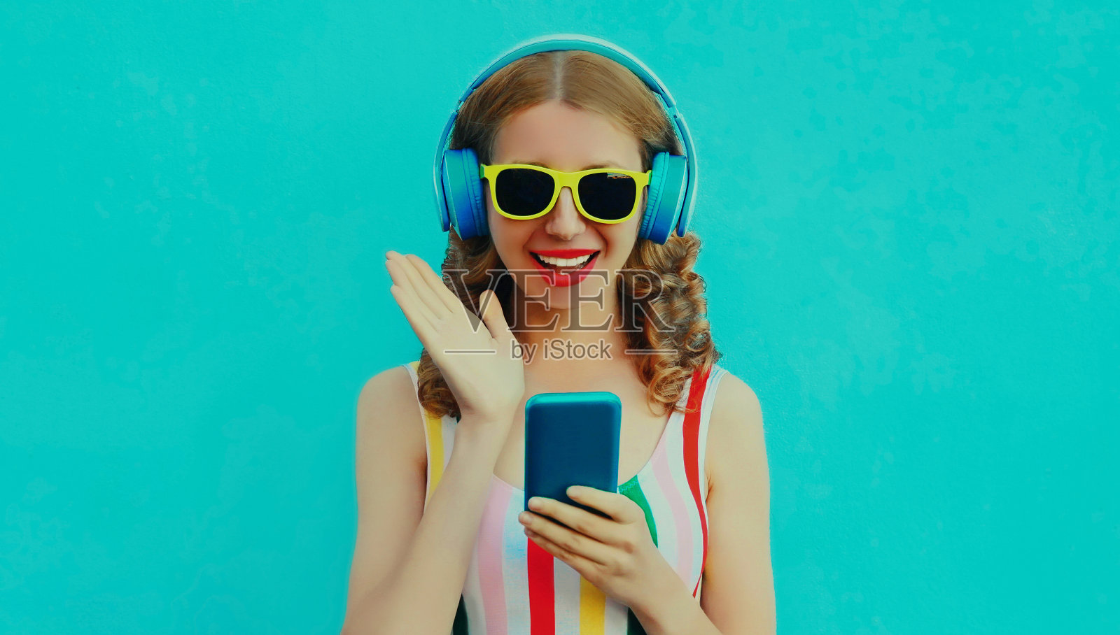 快乐微笑的年轻女子的肖像在无线耳机与手机听音乐的蓝色背景照片摄影图片