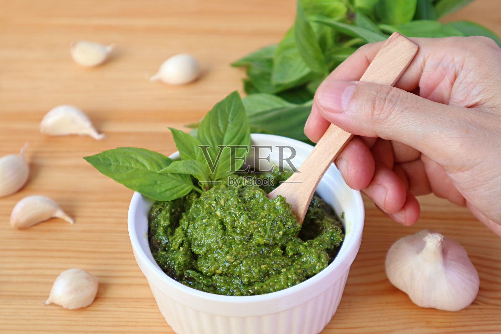 男子手握木勺从白碗中舀出新鲜罗勒香蒜酱照片摄影图片