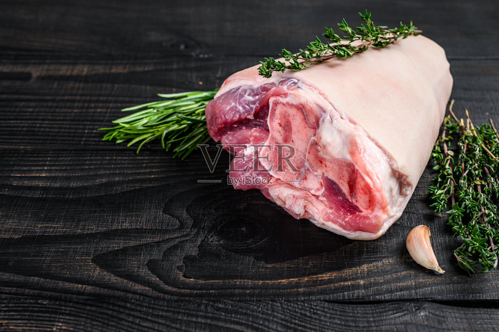 生猪肘腿肉放在厨房的桌子上，配上香草。黑色木制背景。前视图。本空间照片摄影图片