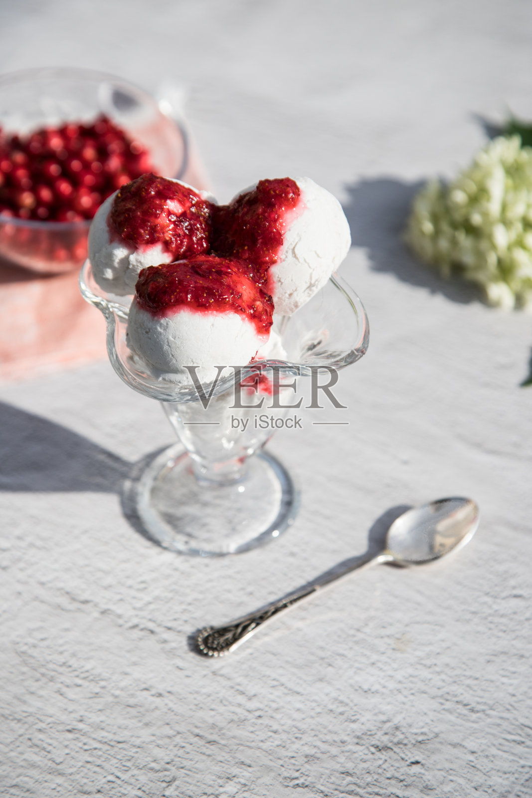 玻璃碗里装着冰淇淋球，背景上放着蔓越莓果酱，玻璃碗里装着浆果，桌子上有太阳的影子。垂直方向照片摄影图片