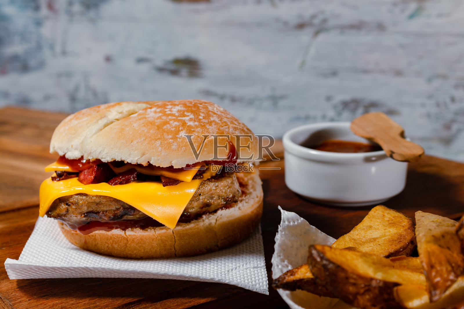 美味的汉堡与切达奶酪和烤熏培根自制面包配上壮观的乡村土豆和自制烧烤酱。照片摄影图片