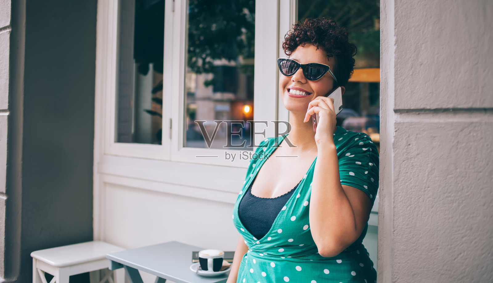 时尚的非洲裔美国女士在休闲穿戴和太阳镜享受在户外咖啡馆智能手机聊天照片摄影图片