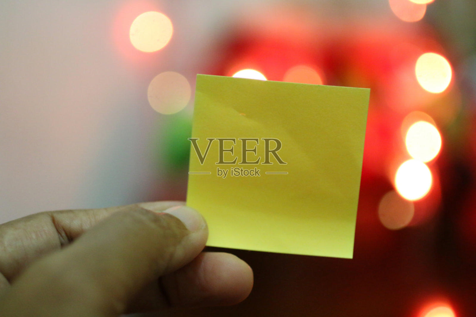 手里拿着空白的黄色纸和彩色的散景背景。照片摄影图片