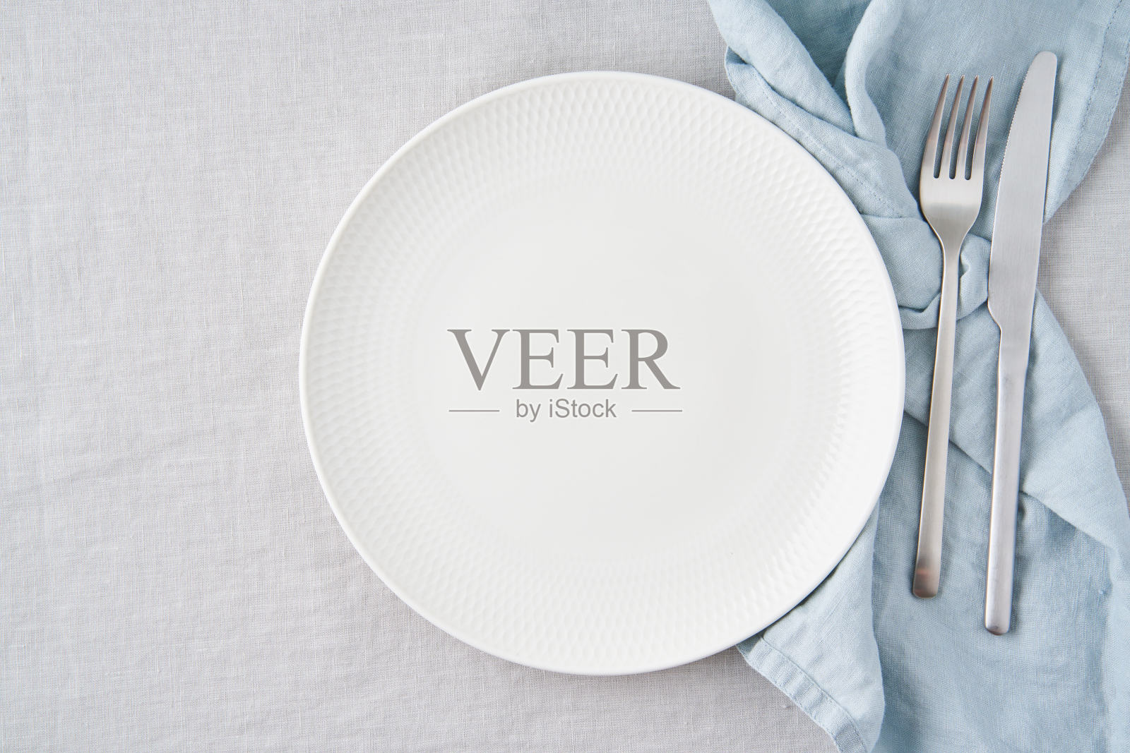 干净的白色盘子，刀叉放在灰色亚麻布桌布上，复制空间照片摄影图片