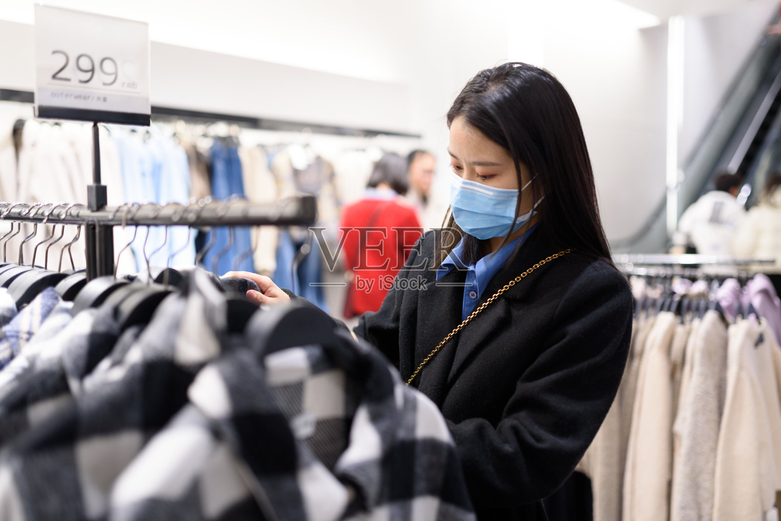 年轻的亚洲妇女戴着防护面具，在一家精品店挑选衣服。2019冠状病毒病大流行期间的生活方式。照片摄影图片