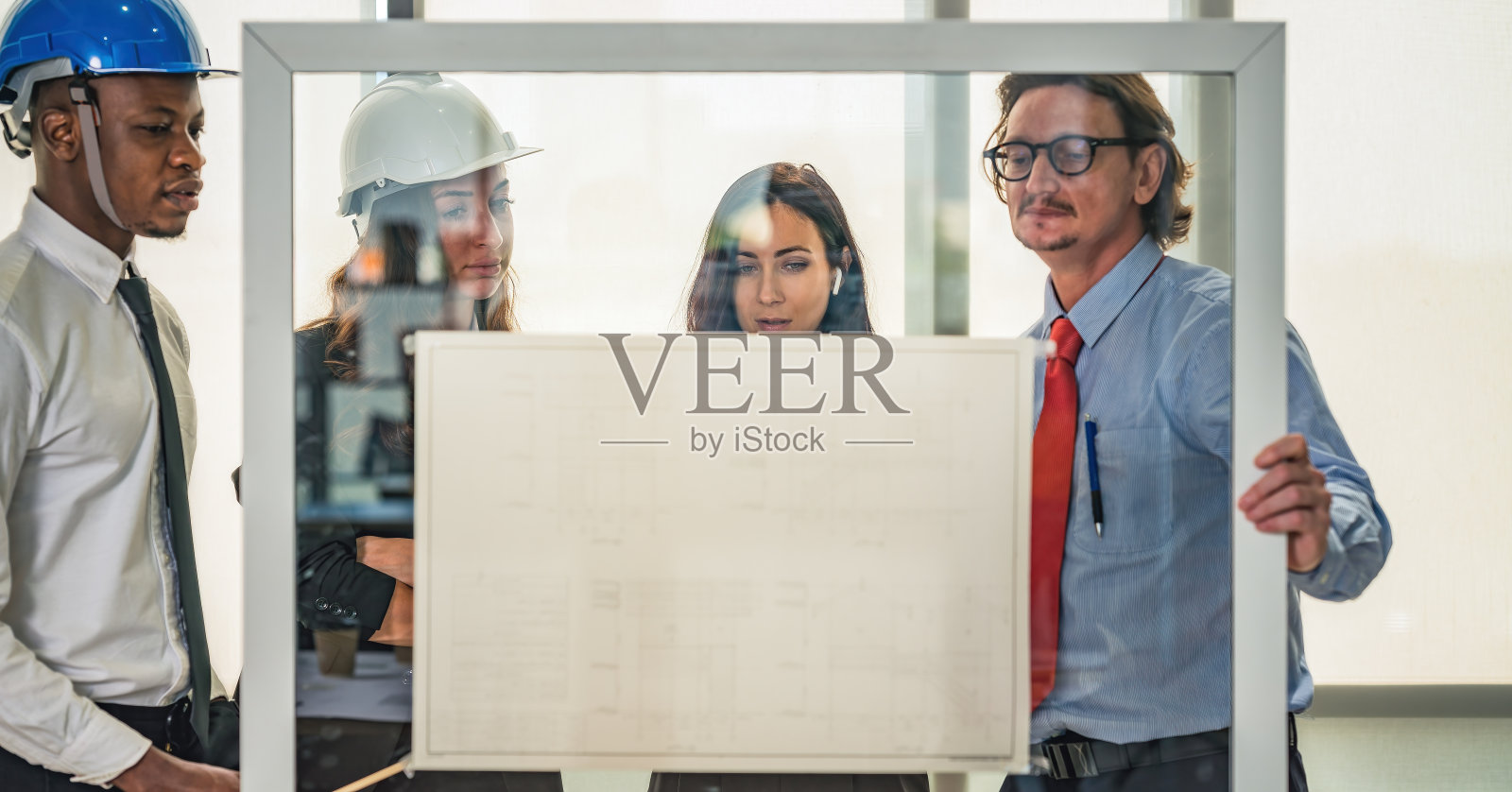 具有建筑和工程业务背景的建筑师和工程师项目开发团队，在建筑师办公室与玻璃板上的项目平面图进行头脑风暴照片摄影图片