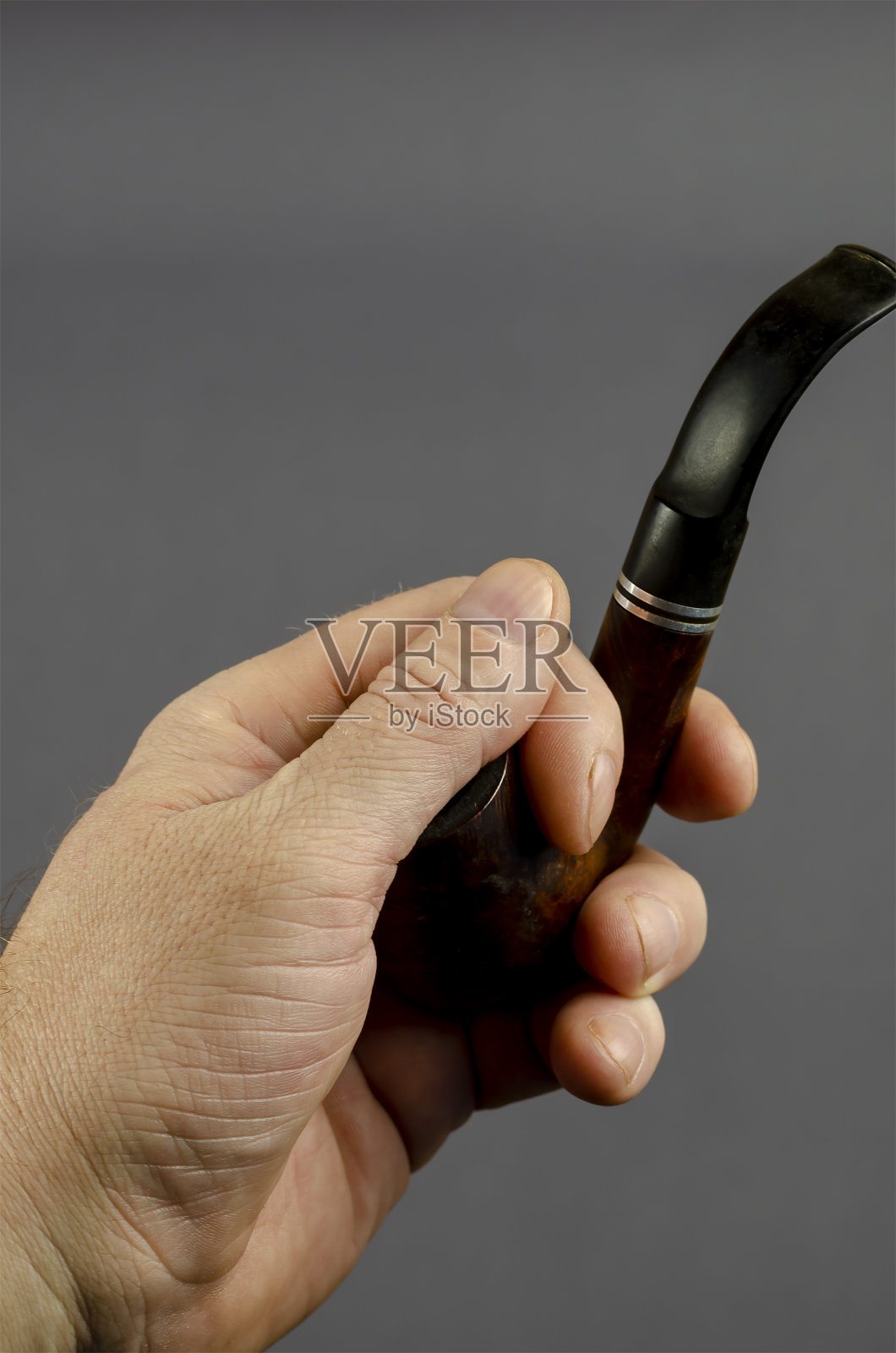 手拿着烟斗，灰色背景。照片摄影图片