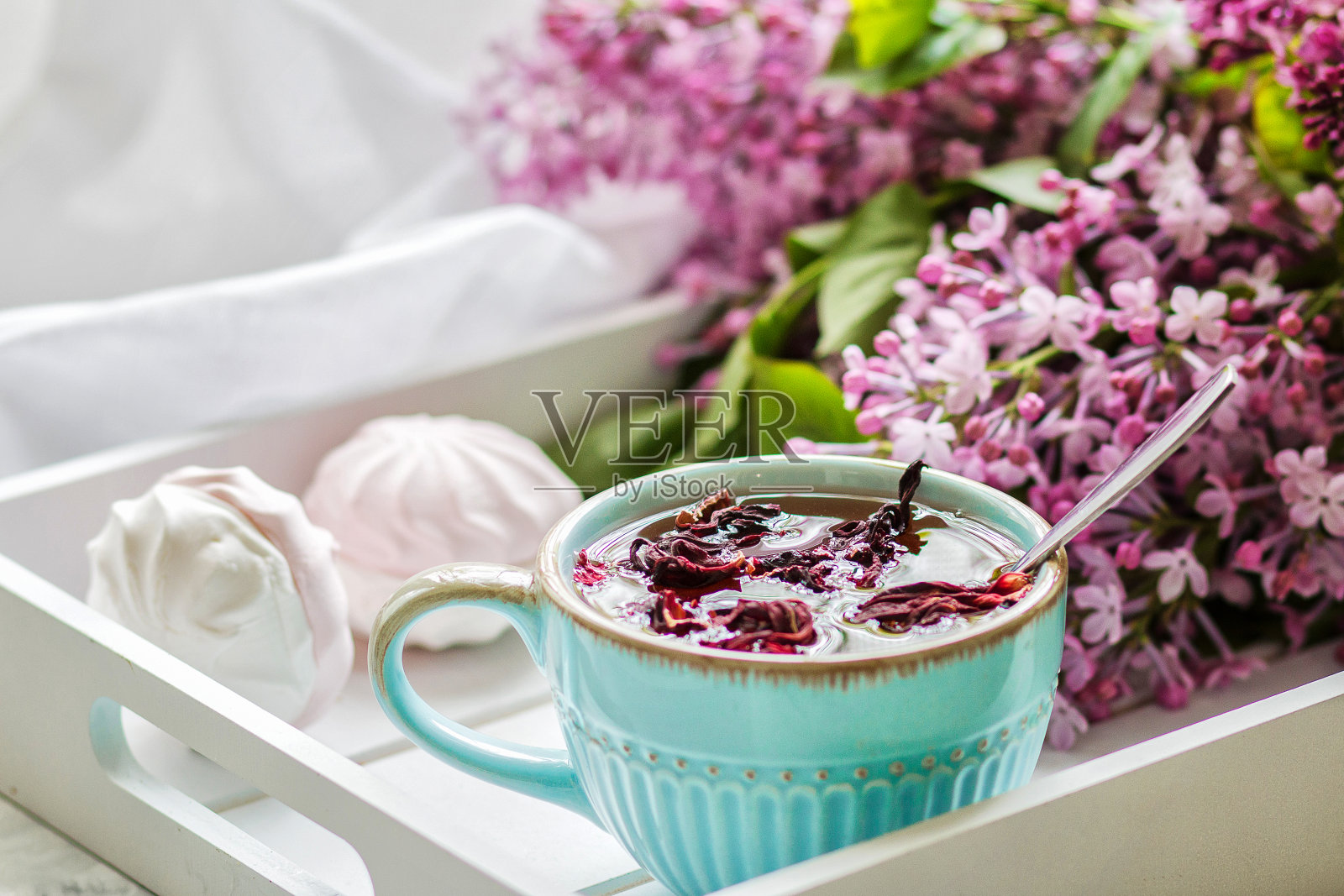 蓝色瓷杯里放着芙蓉茶，白色木托盘上放着自制的棉花糖和一束紫丁香。关闭了。照片摄影图片