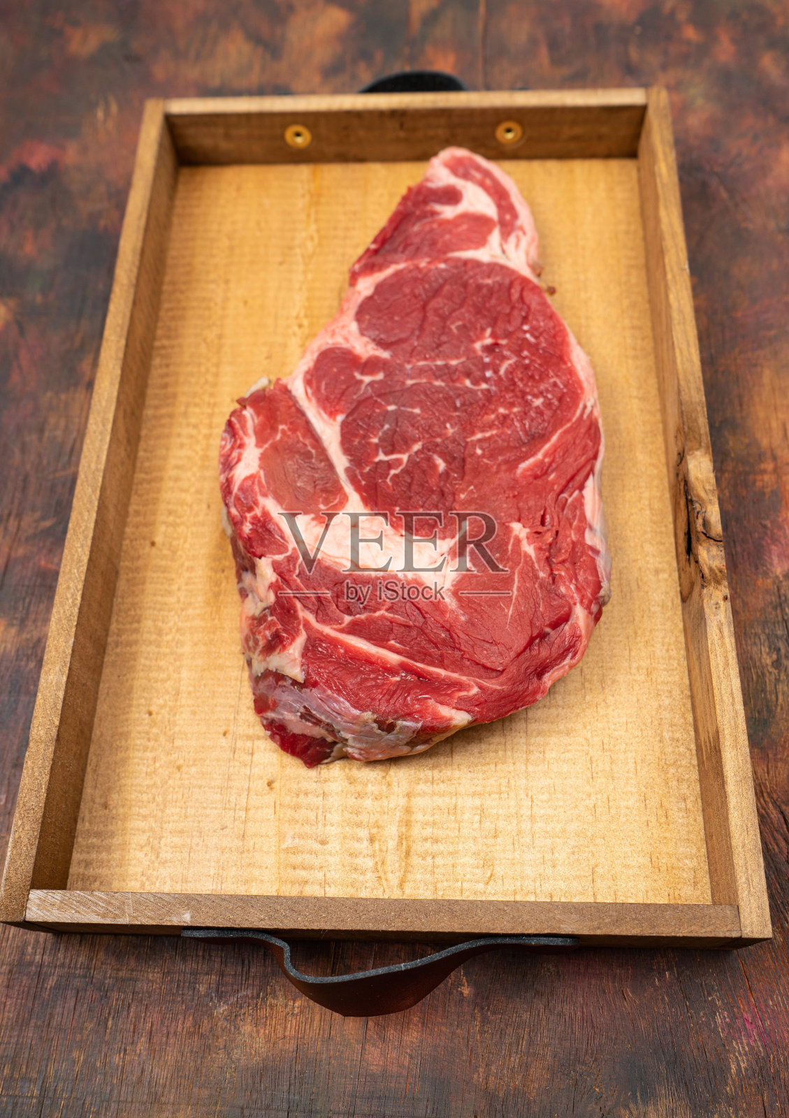 在一张棕色的旧木桌上，一块圆形的石板盘子上放着生牛肉照片摄影图片