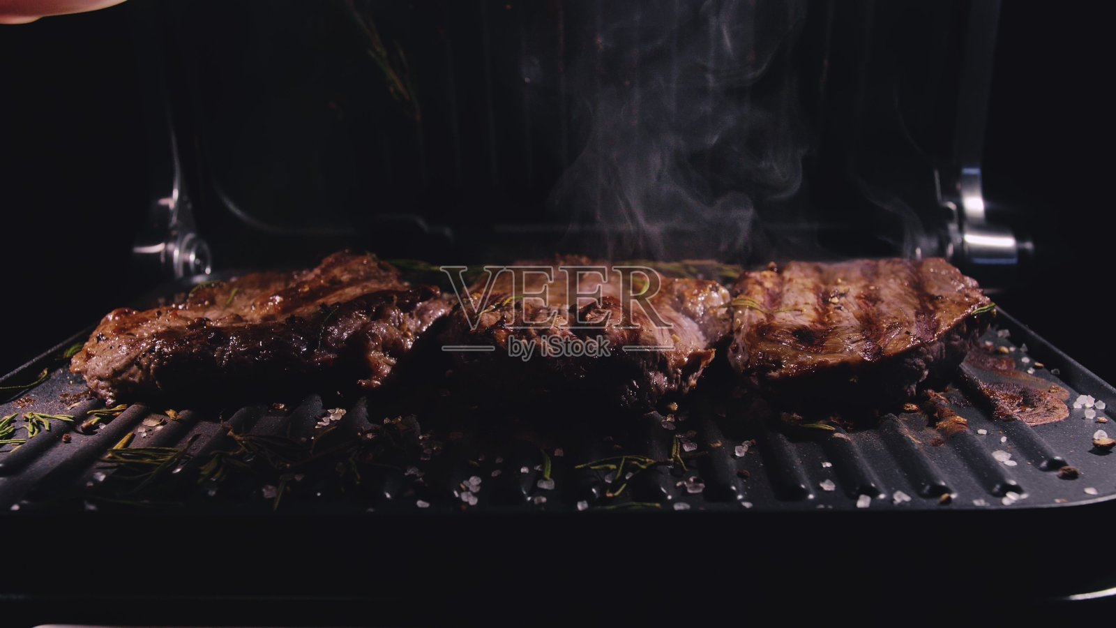 美味多汁的肉排烤制。电烤牛肉，迷迭香，黑胡椒，盐。缓慢的运动。照片摄影图片