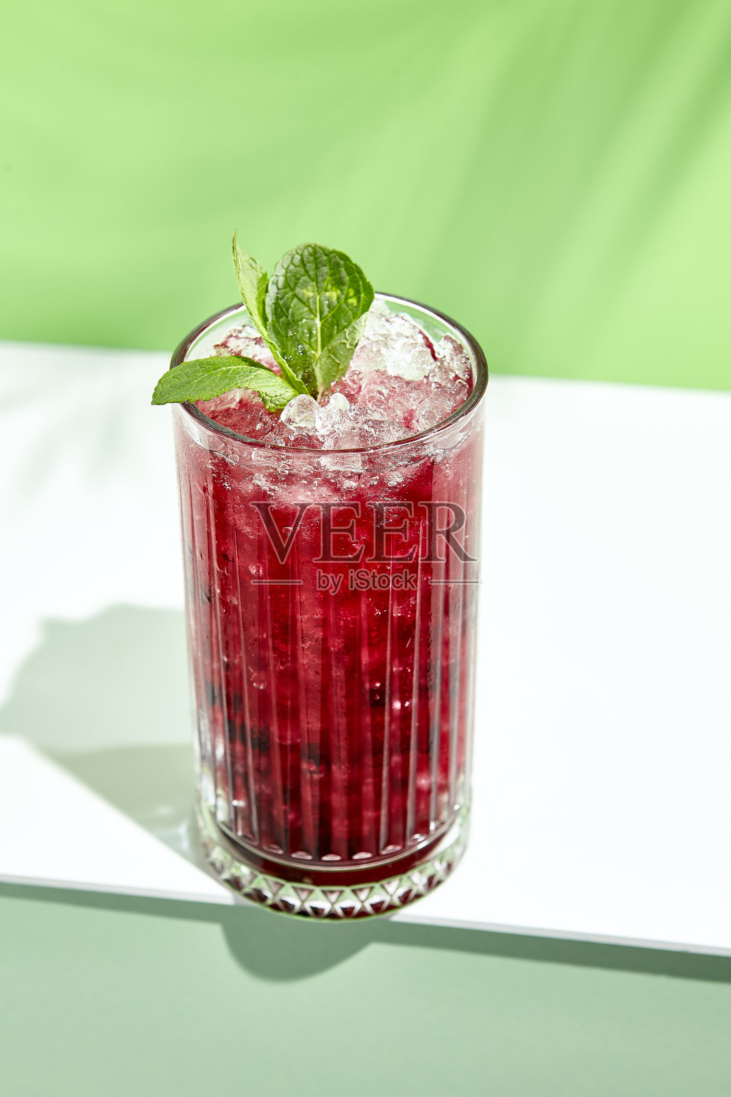 黑加仑柠檬水饮料在绿色的背景。白色的桌子与阳光和棕榈叶坚硬的阴影。夏季，热带和多汁的概念照片摄影图片