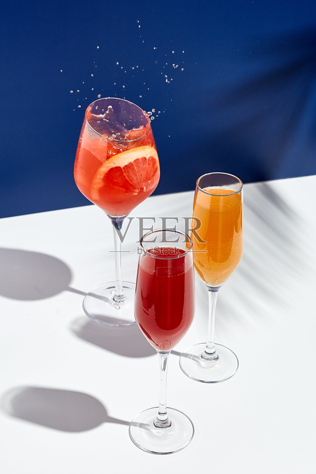 白色桌子，蓝色背景，Aperol饮料和贝里尼鸡尾酒。阳光和棕榈叶影饮现代静物。夏天，派对，热带和新鲜的概念照片摄影图片