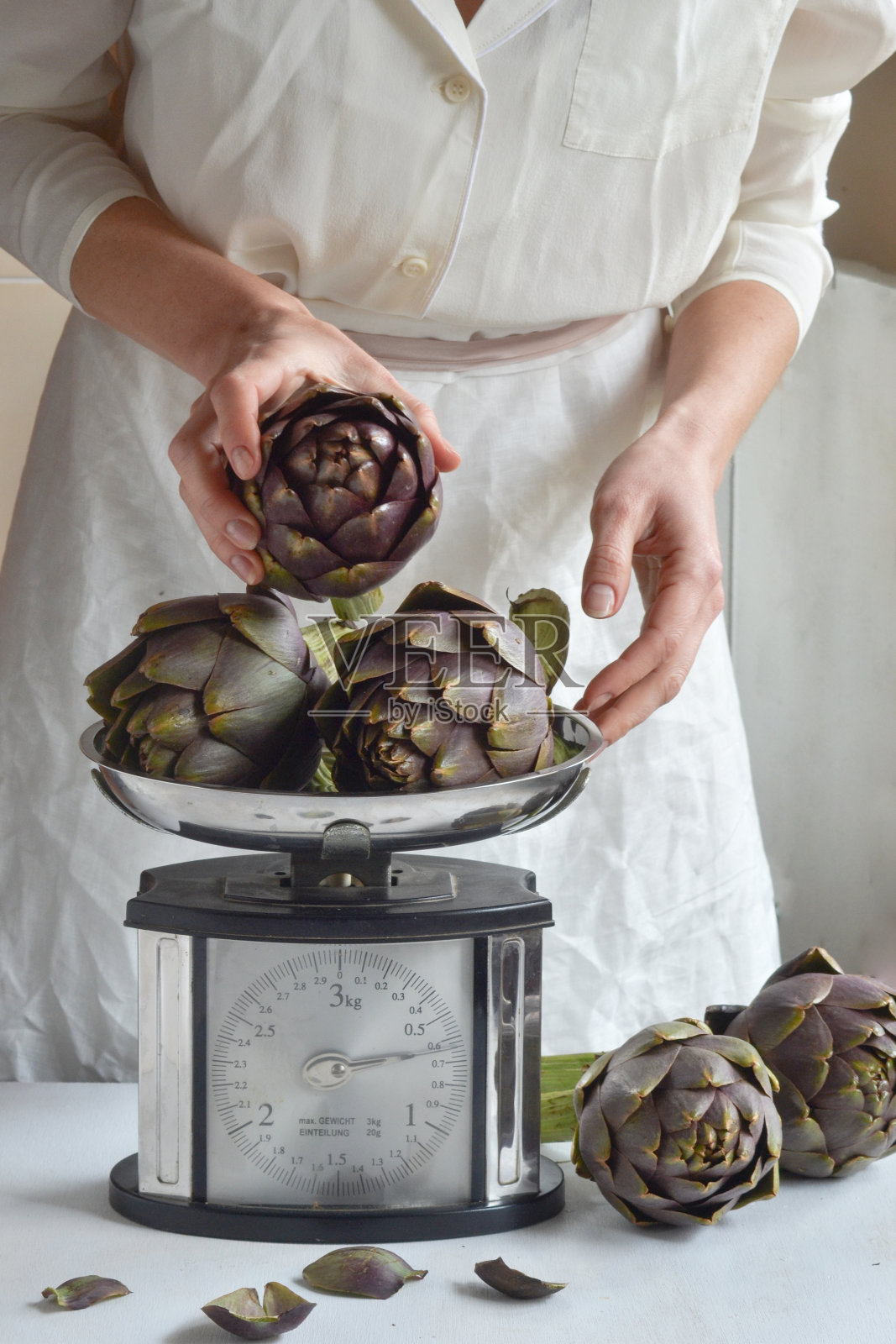 女人把新鲜的洋蓟放在天平上。照片摄影图片